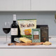 The Wine & Cheese Treat Box. A wooden serving board displays a selection of gourmet items, including a block of cheese, Irish oat cookies, and a packet of Keogh's crisps. Next to the board is a bottle of red wine and a wine glass filled with wine, all set against a modern kitchen backdrop. The Wine & Cheese Treat Box. A wooden serving board displays a selection of gourmet items, including a block of cheese, Irish oat cookies, and a packet of Keogh's crisps. Next to the board is a bottle of red wine and a wine glass filled with wine, all set against a modern kitchen backdrop.